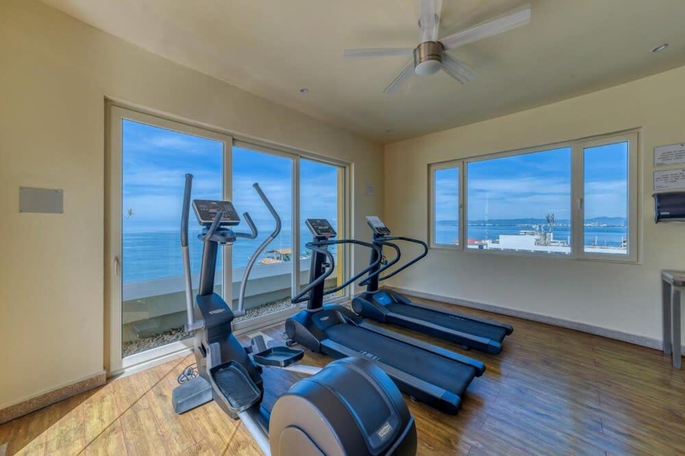 a gym with three cardio machines in a room with windows at Chic Studio -Rooftop Pool - Ocean View - King Bed in Puerto Vallarta