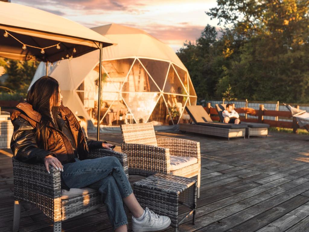 a woman sitting on a chair under an umbrella at Waterfront Glamping - Private hot tube, sauna & sunset view in Wapnica