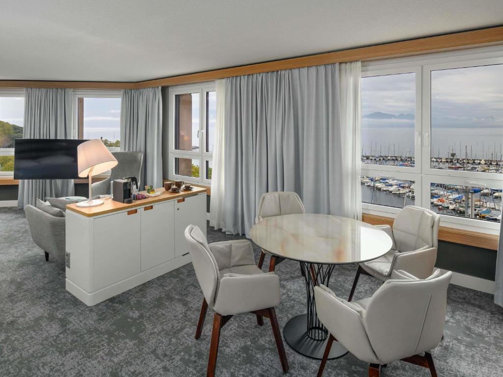 a hotel room with a table and chairs and a desk at Mövenpick Hotel Lausanne in Lausanne