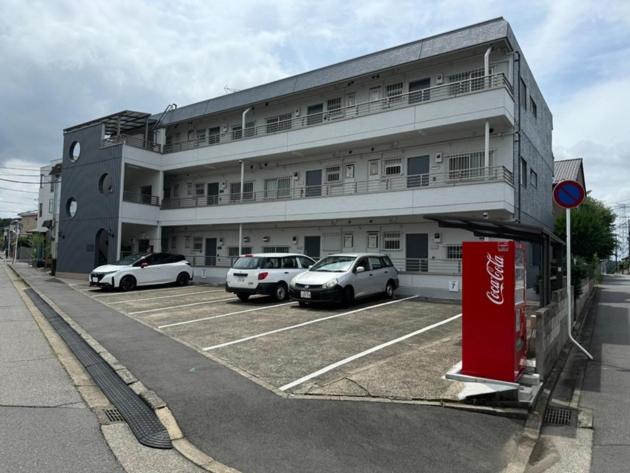 ein Gebäude mit auf einem Parkplatz geparkten Autos in der Unterkunft HYGGE HOUSE Tabibitonoie - Vacation STAY 61141v in Kashiwa