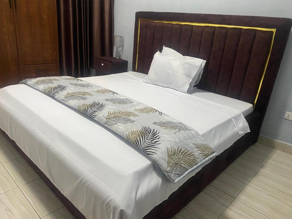 un lit avec des draps blancs et une tête de lit en bois dans l'établissement KIGALI AIRPORT TRANSIT RESIDENCe, à Kigali
