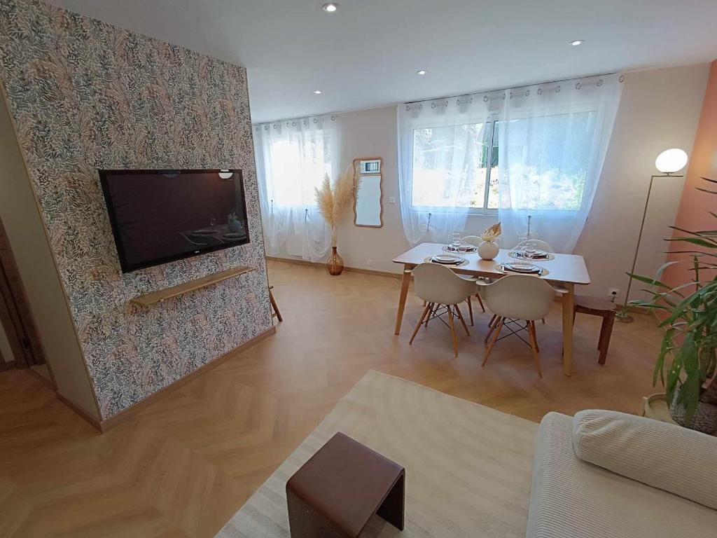 Una sala de estar con una mesa y un televisor en una pared. en Le Lila, en Cholet
