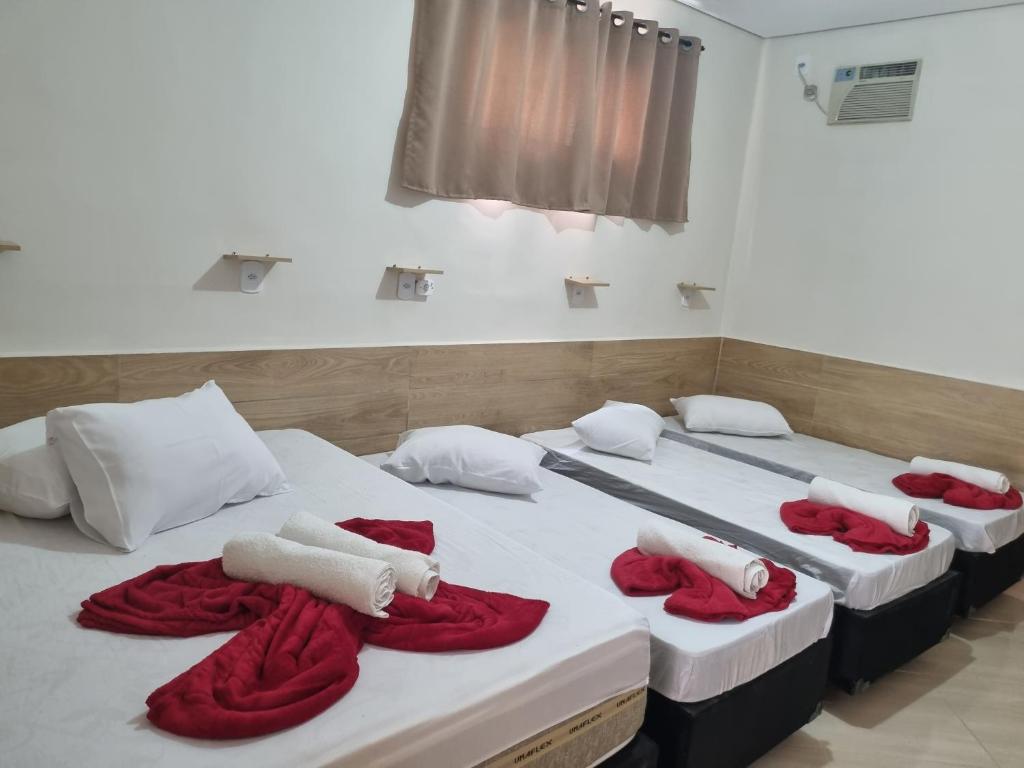 three beds in a room with red and white towels on them at Pousada Quarto tv Smart ar Garagem Gratuita in Aparecida