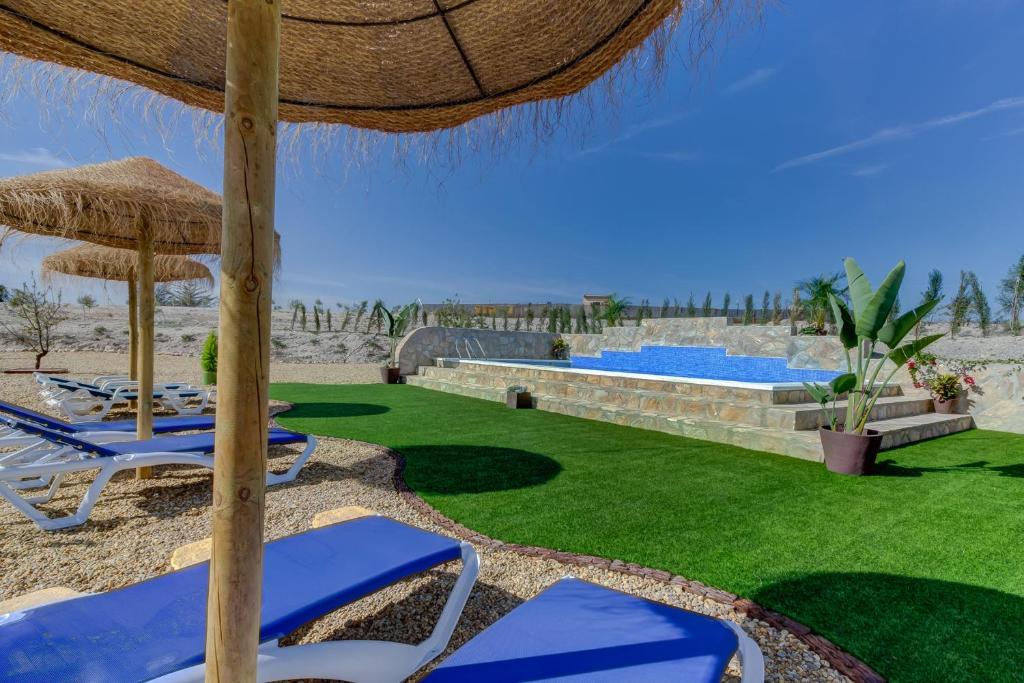 a lawn with chairs and an umbrella and a swimming pool at Villa Damara in Albox