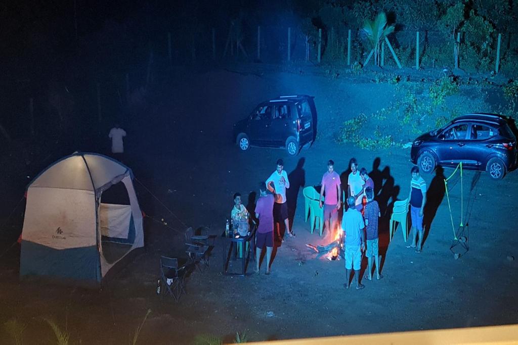 a group of people standing around a fire next to a tent at Hotel O Home Bhogwal Farmhouse & Party Zone in Chinchavli