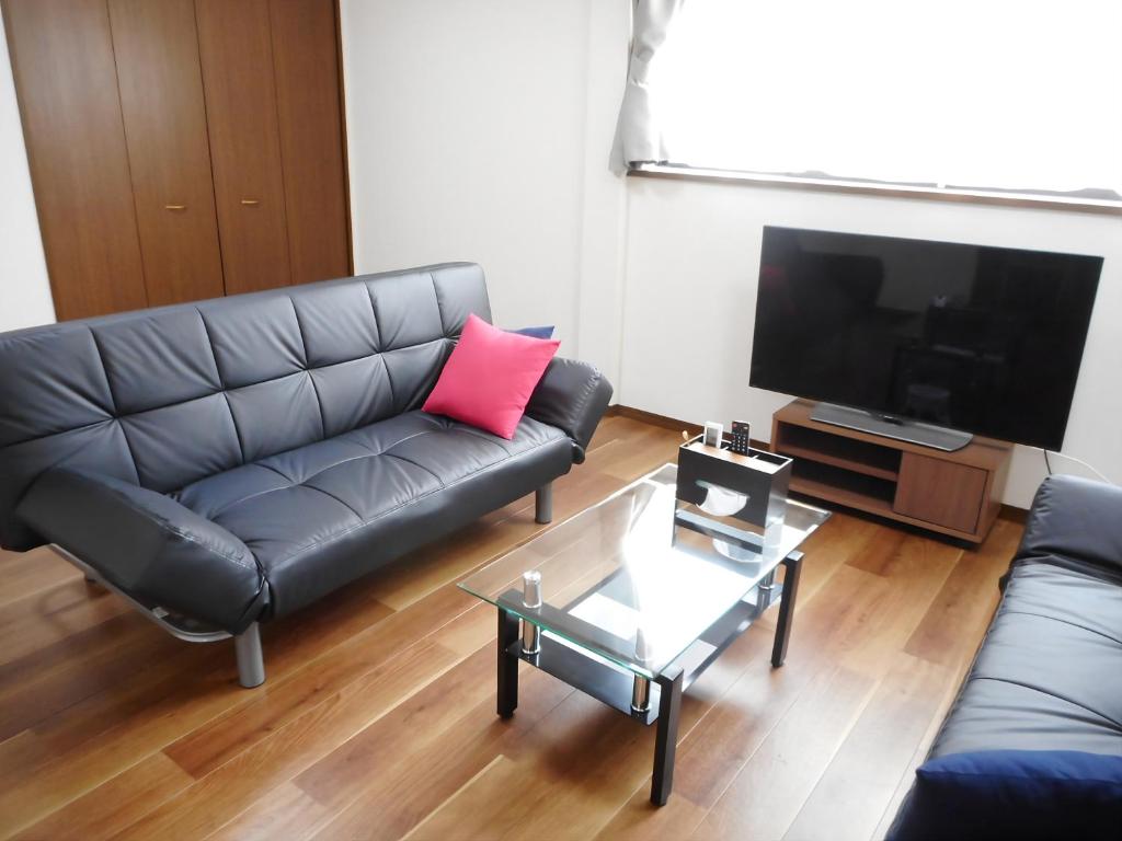a living room with a black leather couch and a tv at Bhome Hikone Jizo in Hikone