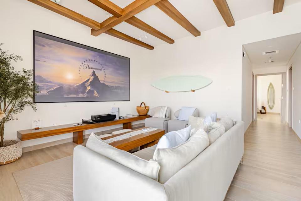 a living room with white furniture and a large screen at The Surfer's Yas 2BR plus Study Apartment, Full canal & pool view, Theme Parks Yas in Yas Island