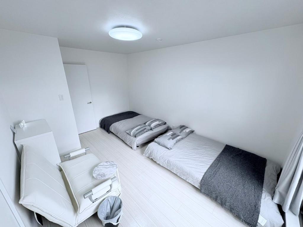 ein weißes Zimmer mit 2 Betten und einem Stuhl in der Unterkunft G-stay in Wada