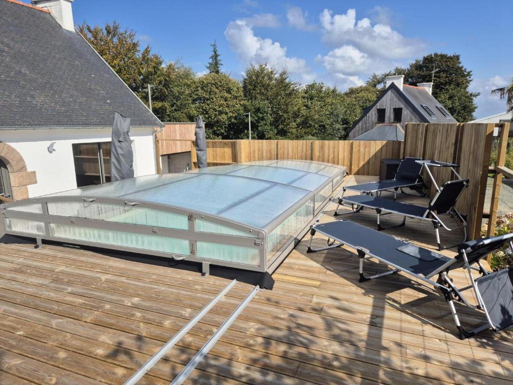 a glass swimming pool on a deck with two chairs at Ty gouldri in Saint-Quay-Perros
