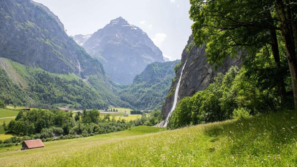 a valley with a waterfall and a mountain at Gemütliche Ferienwohnung Bergzyt - oder Bed and Breakfast , Tradition trifft Gemütlichkeit - Ski und Wandergebiet in Linthal