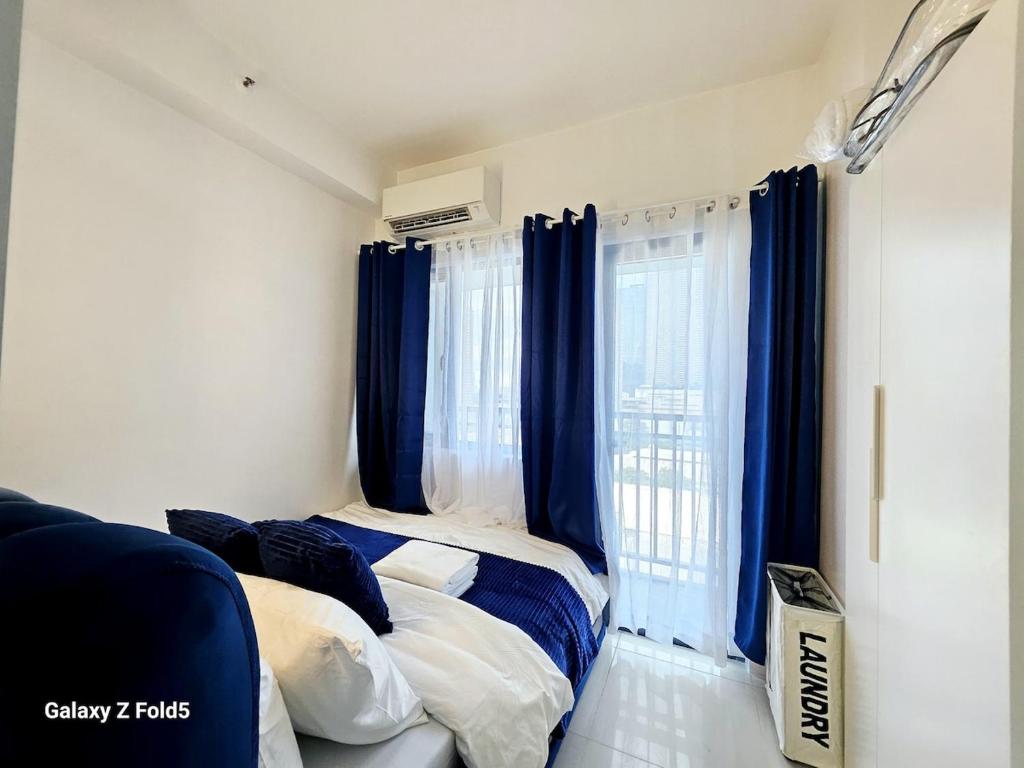 a bedroom with two beds and blue curtains at Affordable Condotel near Sm Megamall with Fast WiFi in Sampong