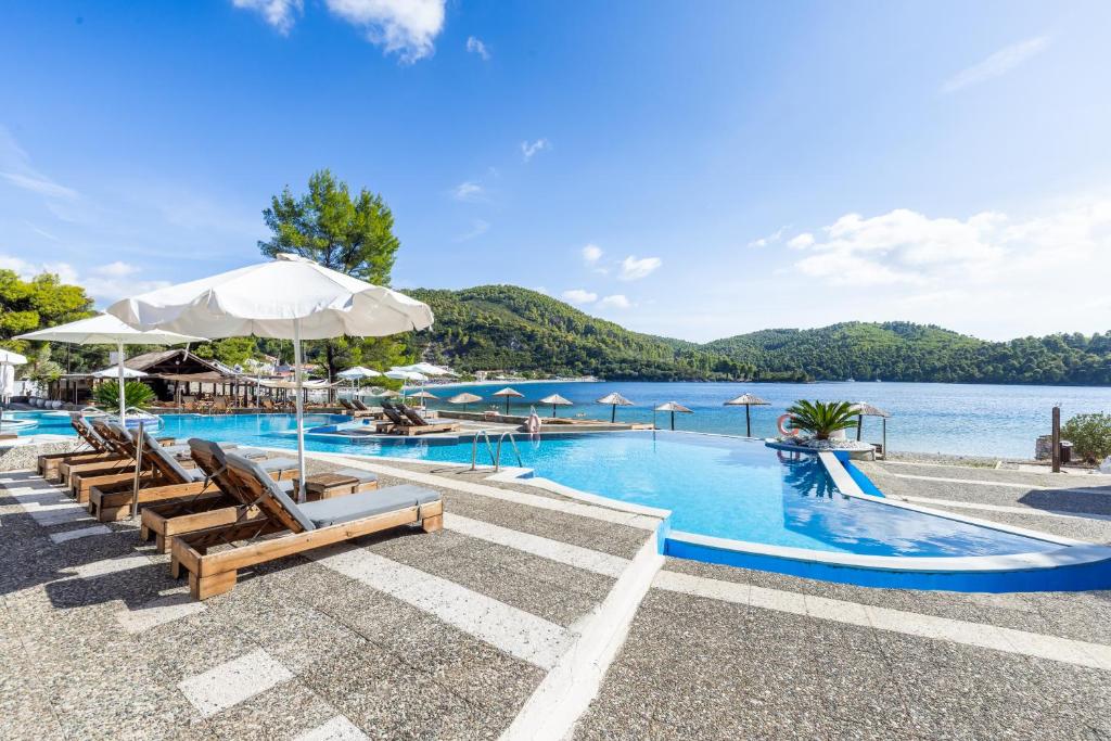 a pool with chairs and umbrellas next to a lake at Blue Green Bay in Panormos Skopelos