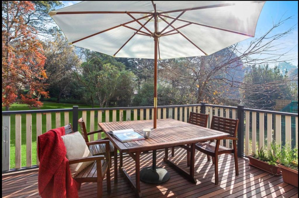 einem Holztisch mit einem Sonnenschirm auf dem Deck in der Unterkunft Korla Cottage, Leura Family & Pet Friendly Stay in Leura