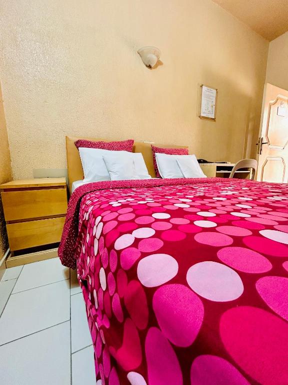 ein Schlafzimmer mit einer rosa Bettdecke auf einem Bett in der Unterkunft Hôtel Saint Thomas in Lomé
