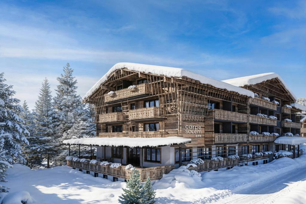 un grand bâtiment en bois recouvert de neige dans la neige dans l'établissement Carpe Solem Kaprun Apartments 4 stars by ALPS RESORTS, à Kaprun