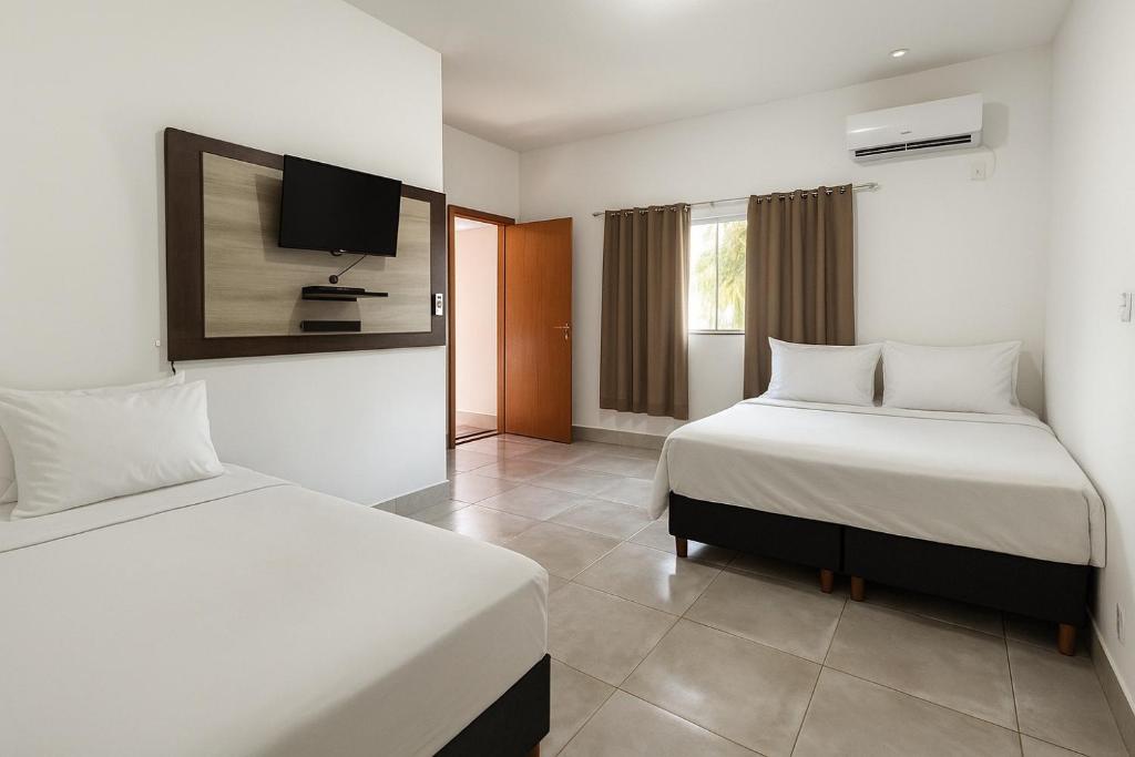 a bedroom with two beds and a tv on the wall at A Casa Paradisíaca Total Luxuoso Piscina Super Hiper Mega Quente 50 graus Aquecimento Elétrico , Sinuca e 5 Quartos Com Ar Condicionado Com Roupa de Cama e Banho in Caldas Novas