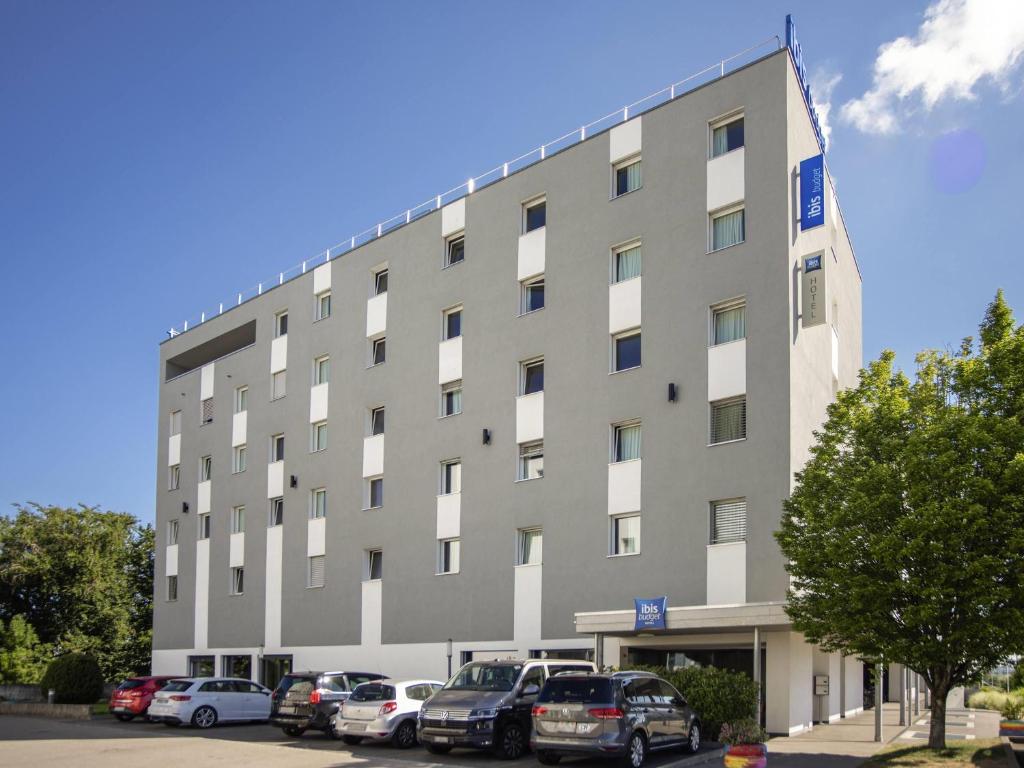 a large building with cars parked in a parking lot at ibis budget Fribourg in Fribourg