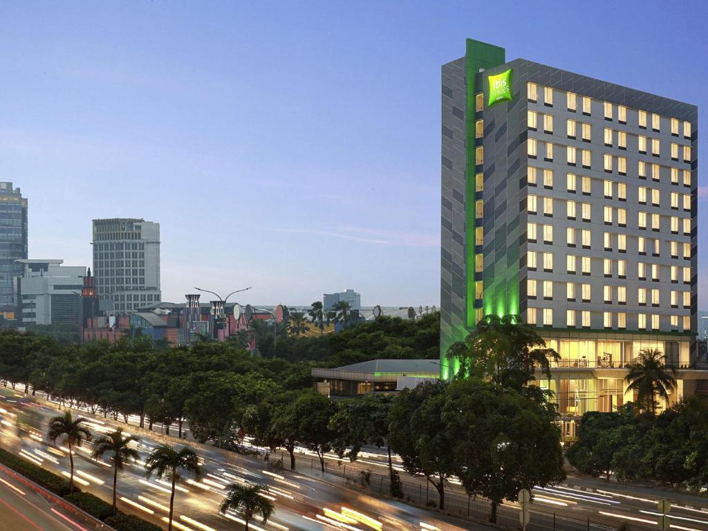 un edificio alto con un letrero verde al lado de una calle en ibis Styles Jakarta Simatupang, en Yakarta