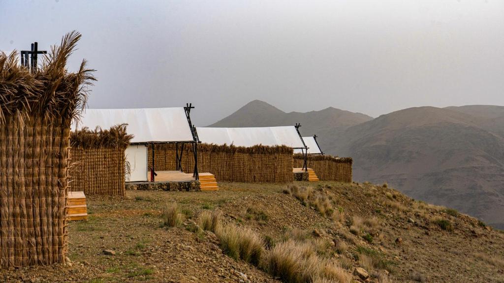 two huts on a hill with mountains in the background at Husaak Tabab Adventure Lodge 