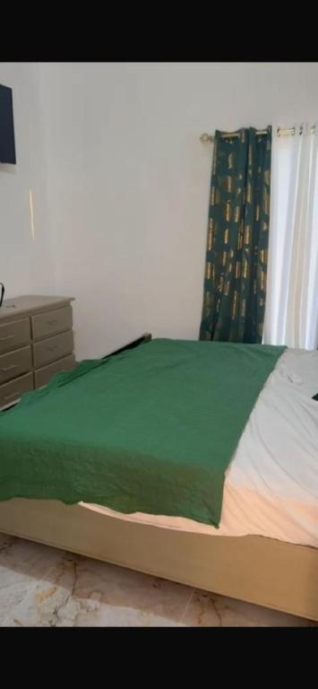 een bed met een groene deken en een ladekast in een slaapkamer bij santo domingo airport villa in Reparto Esther Rosario