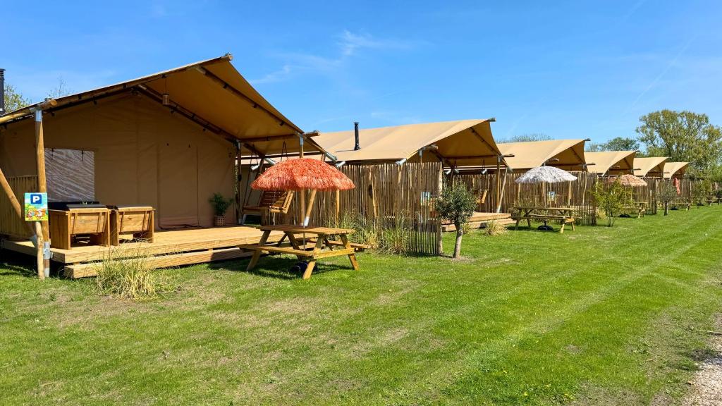 a row of tents with picnic tables and an umbrella at Safari Lodge B in Petten
