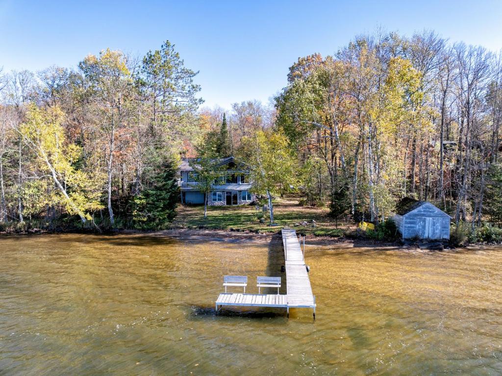 Dos sillas sentadas en un muelle en el agua frente a una casa. en Sandy Shores Condo, en Namekagon