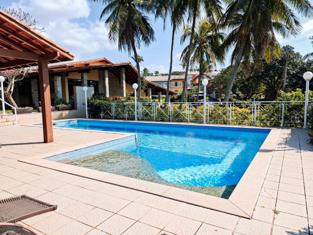 a swimming pool in front of a house with palm trees at Residência hoteleira Aldeia da Praia Guarapari in Guarapari