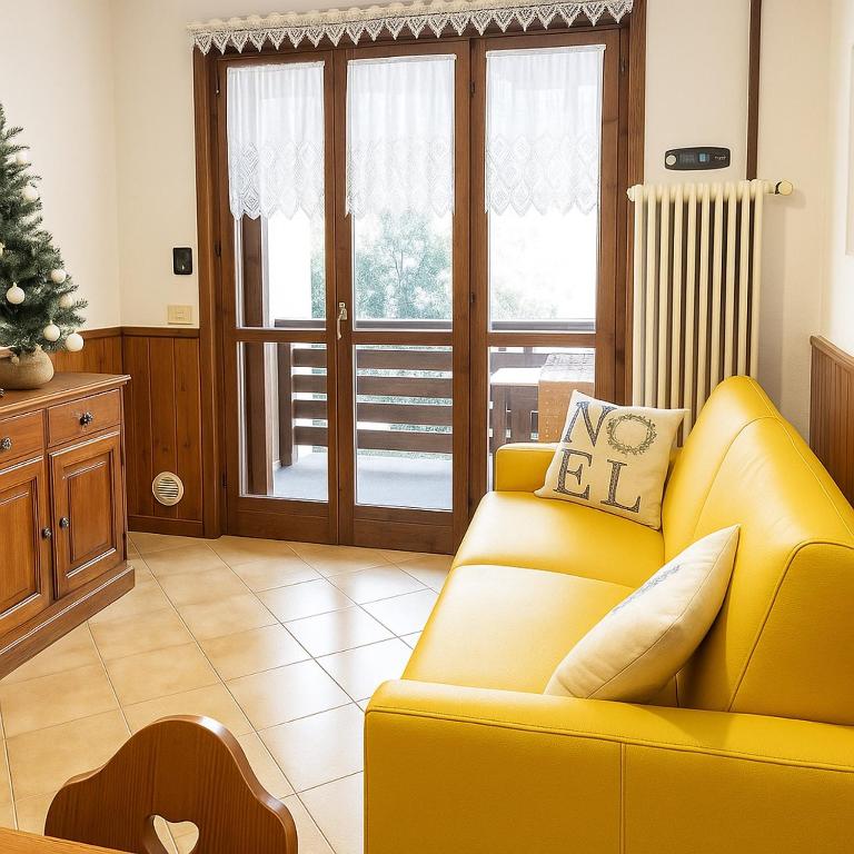 a yellow couch in a living room with a christmas tree at Walk to Slopes & Free Parking -Capriolo Tarvisio in Tarvisio