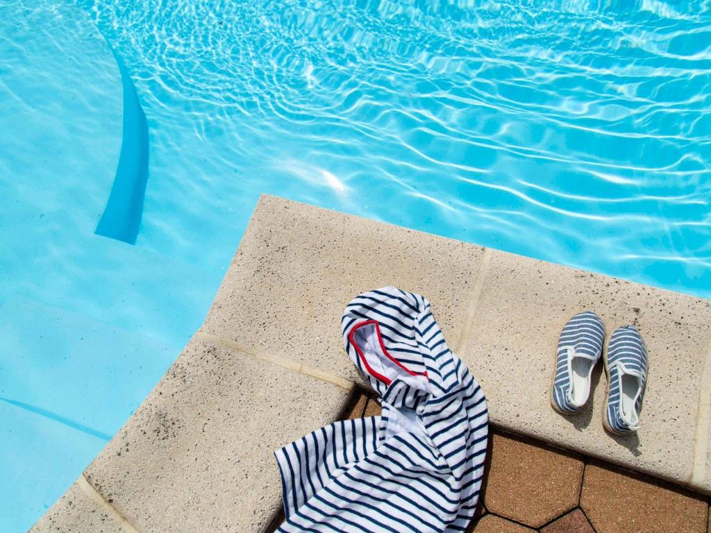une paire de pantoufles à côté d'une piscine dans l'établissement Hôtel ibis Styles Auxerre Nord, à Auxerre