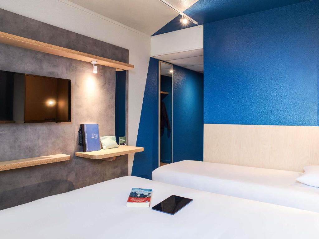 a room with two beds and a blue wall at Hôtel Ibis Budget Nantes Ouest Atlantis Couëron in Couëron