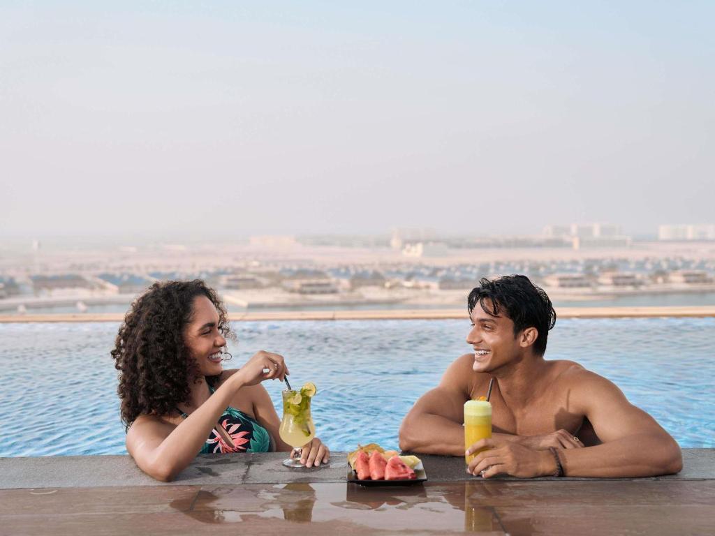 Un hombre y una mujer sentados en el agua con comida y bebidas. en Aparthotel Adagio Dubai Deira, en Dubái
