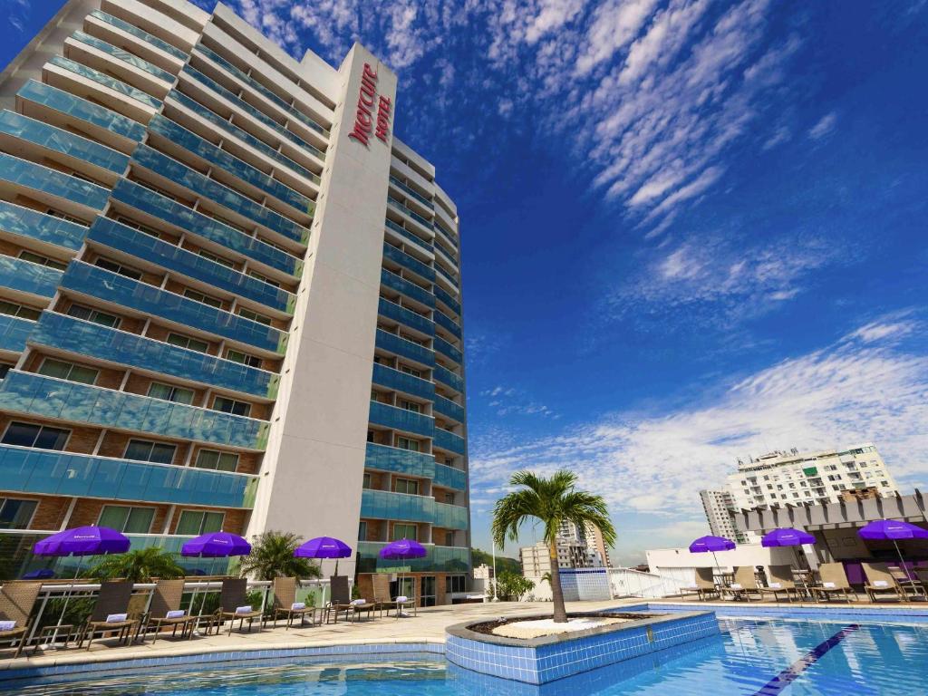un hotel con piscina, sillas y sombrillas púrpuras en Mercure Rio de Janeiro Nova Iguaçu, en Nova Iguaçu