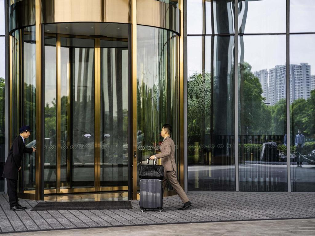 杭州市にあるSofitel Hangzhou Yingguan-Olympic Center Hotelの荷物を持ってガラス張りの建物の前を歩いている男性