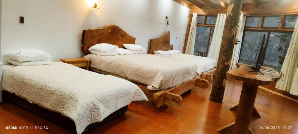 two beds in a room with wooden floors and windows at Altos quiñenahuin lodge in Curarrehue