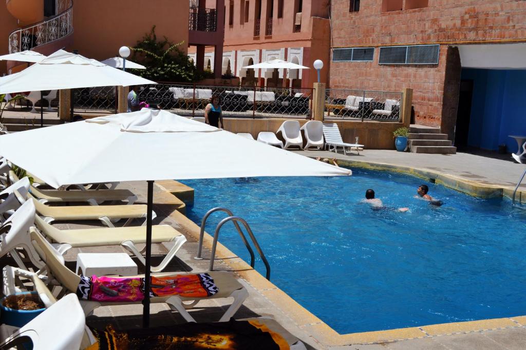 2 personas nadando en una piscina con sombrilla en Le Grand Hotel Tazi, en Marrakech