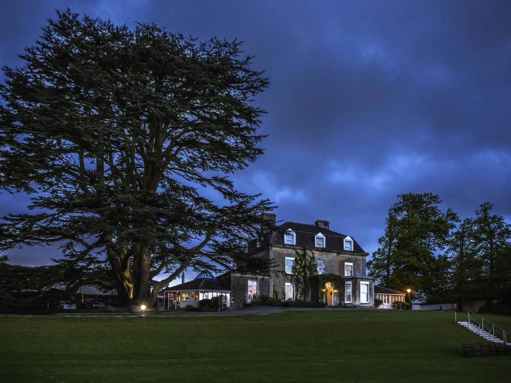 a large house with a large tree in front of it at Mercure Bristol North The Grange Hotel in Bristol