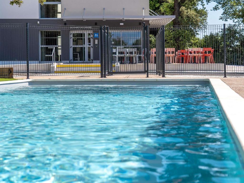 una piscina con acqua blu di fronte a un edificio di ibis budget Le Cannet des Maures a Le Cannet-des-Maures