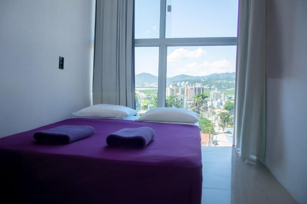 a purple bed with two pillows and a large window at MEG House Hostel in Florianópolis