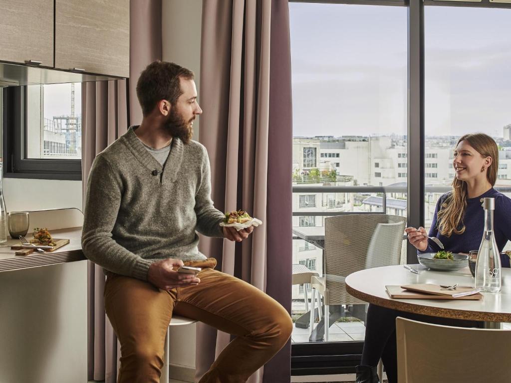 a man and a woman sitting at a table eating food at AppartHotel Mercure Paris Boulogne in Boulogne-Billancourt