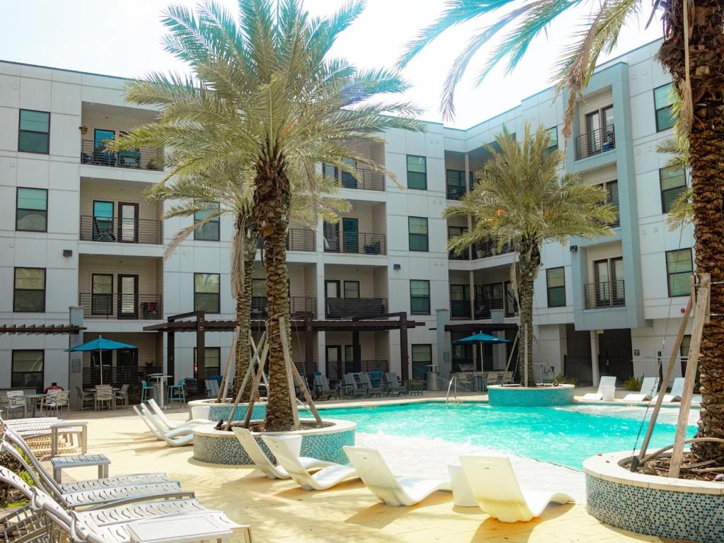 a pool with chairs and palm trees in front of a building at New! The Vibe Med Center Apartments - Central Houston in Houston