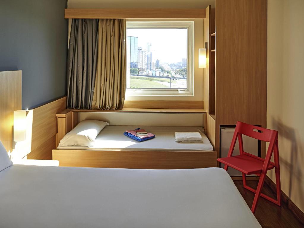 a bedroom with a bed and a window and a red chair at ibis Sorocaba in Sorocaba