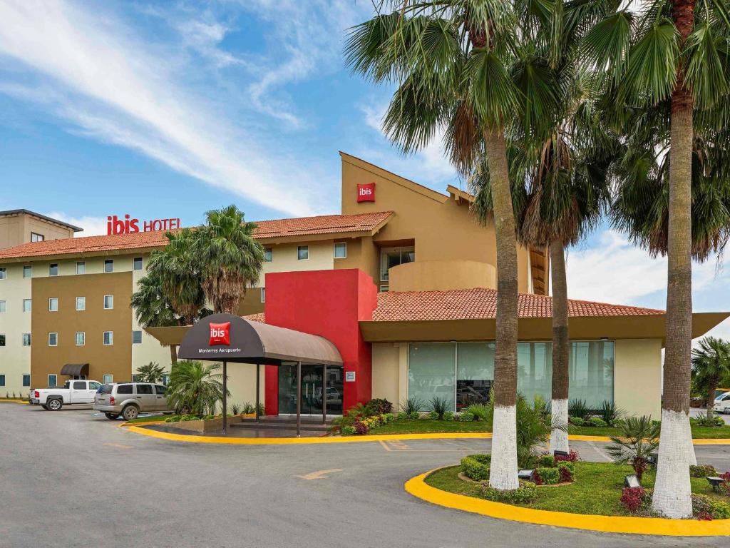 a hotel with palm trees in front of a parking lot at Ibis Monterrey Aeropuerto in Monterrey