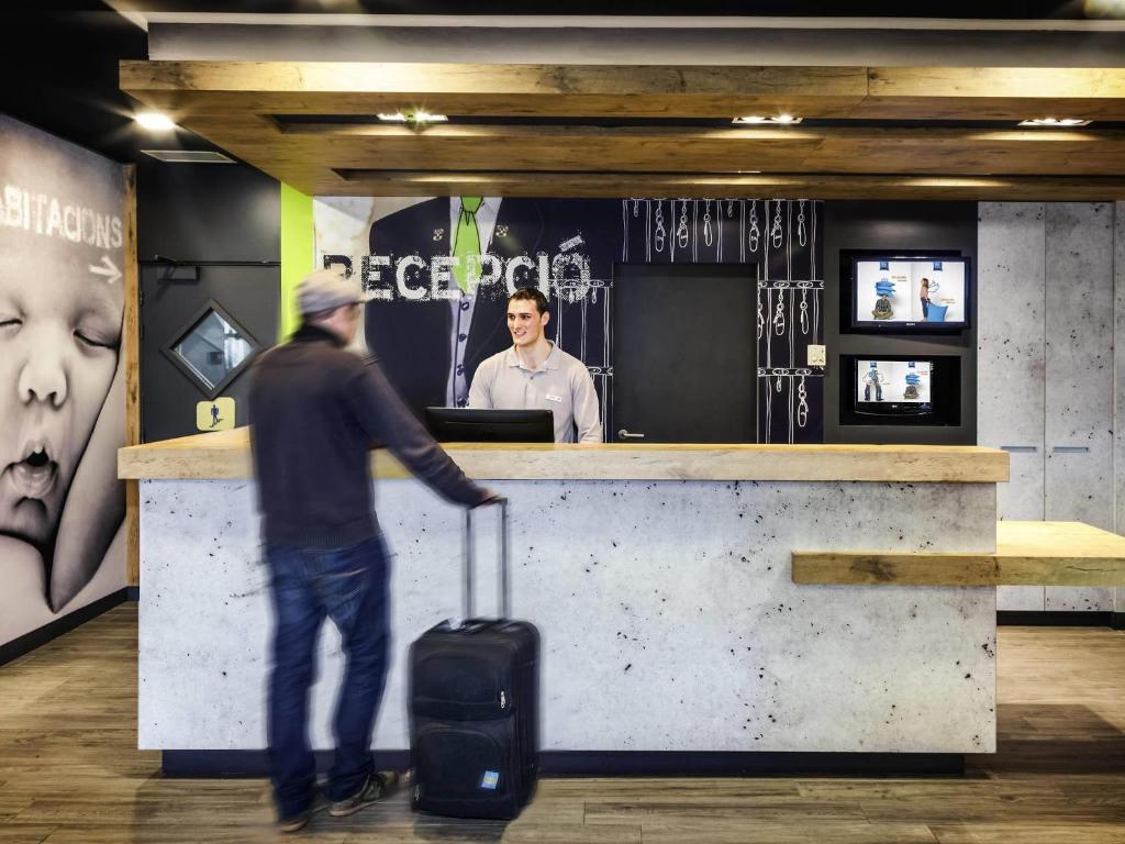 a man walking past a counter with a suitcase at Ibis Budget Barcelona Sant Andreu De La Barca in Sant Andreu de la Barca