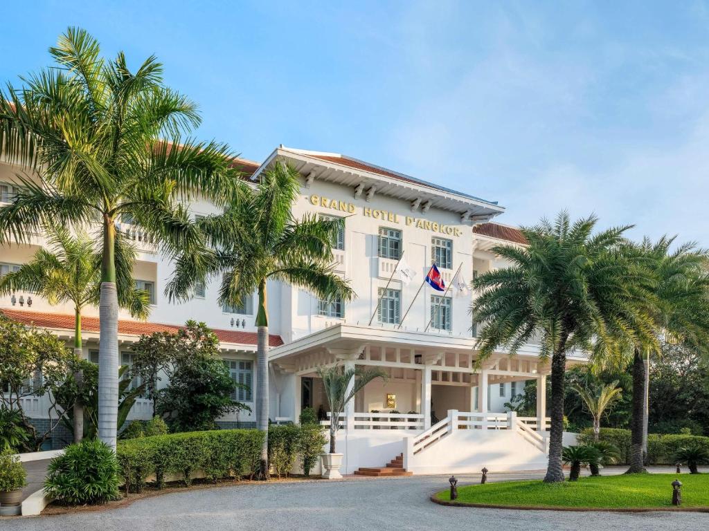 a hotel with palm trees in front of it at Raffles Grand Hotel d'Angkor in Siem Reap