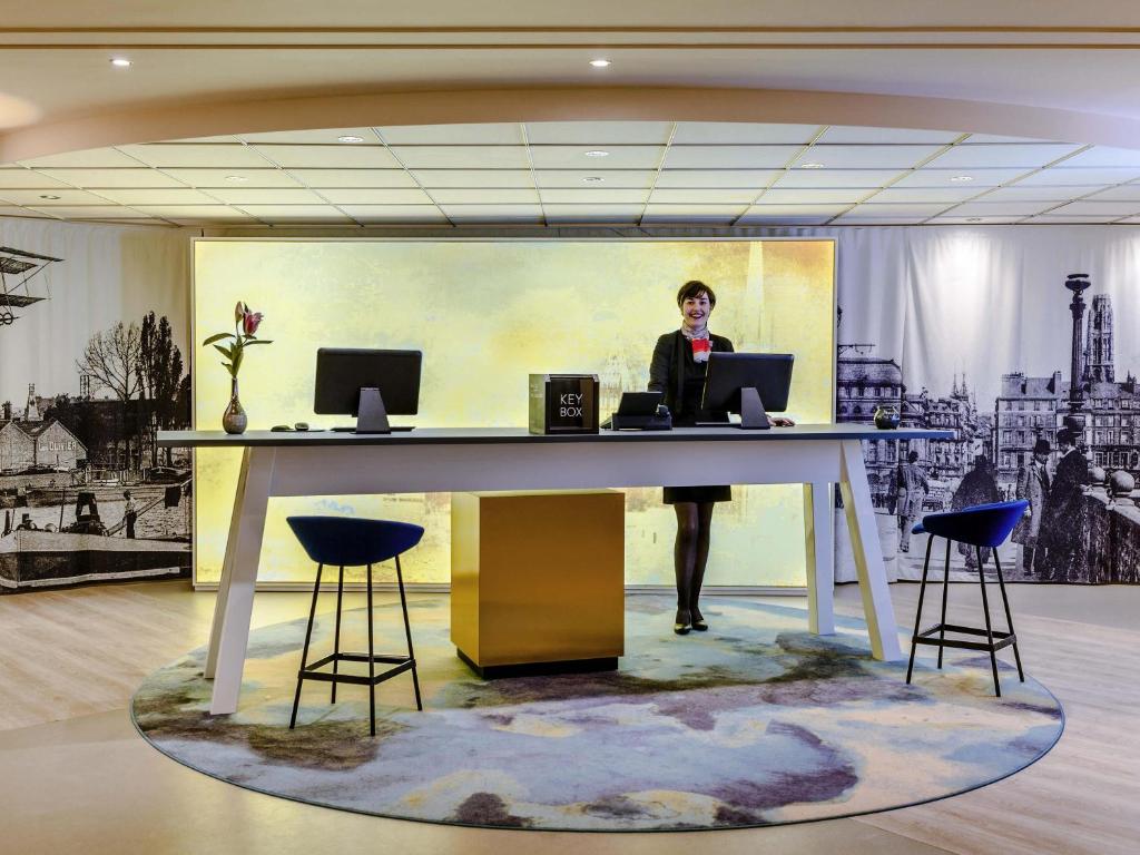 a woman standing at a desk with a laptop at Mercure Rouen Centre Cathédrale in Rouen
