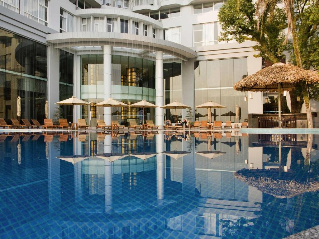 a hotel swimming pool with umbrellas and tables and chairs at Novotel Ha Long Bay Hotel in Ha Long