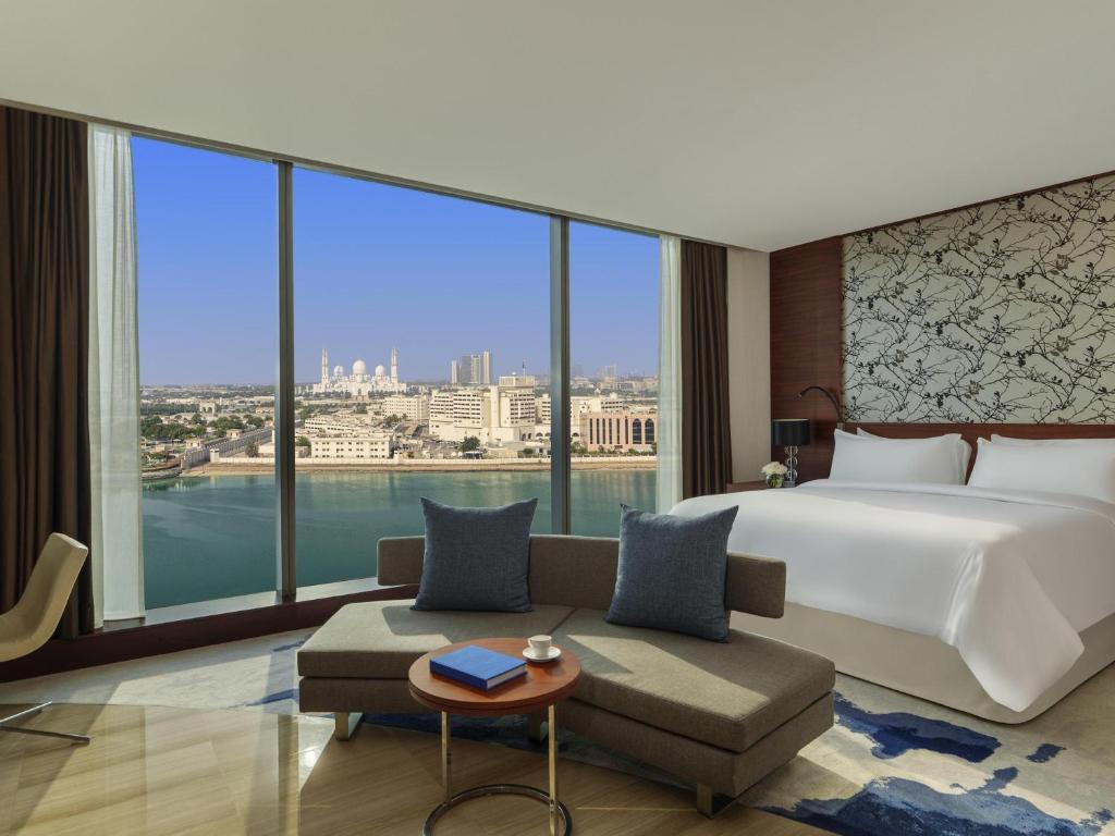 a bedroom with a bed and a couch and a large window at Fairmont Bab Al Bahr in Abu Dhabi