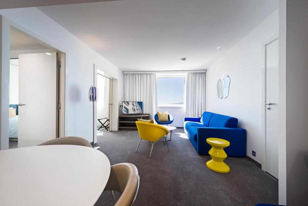 a living room with a blue couch and yellow chairs at Golden Tulip Marseille Euromed in Marseille