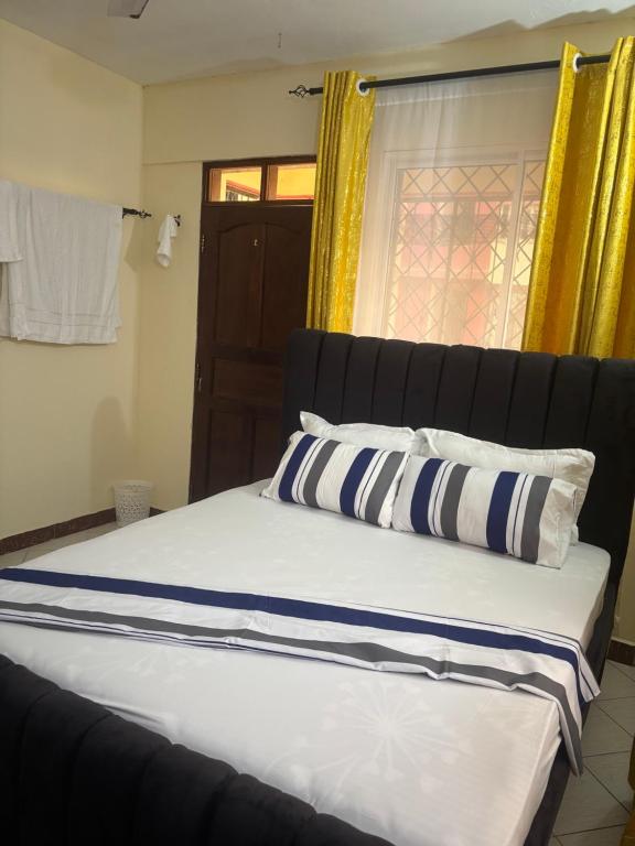 a bed with blue and white pillows and a window at AMTWAPA 2 bedroom pure blissful apartment ready to accommodate you and your family friends or colleagues in Mtwapa