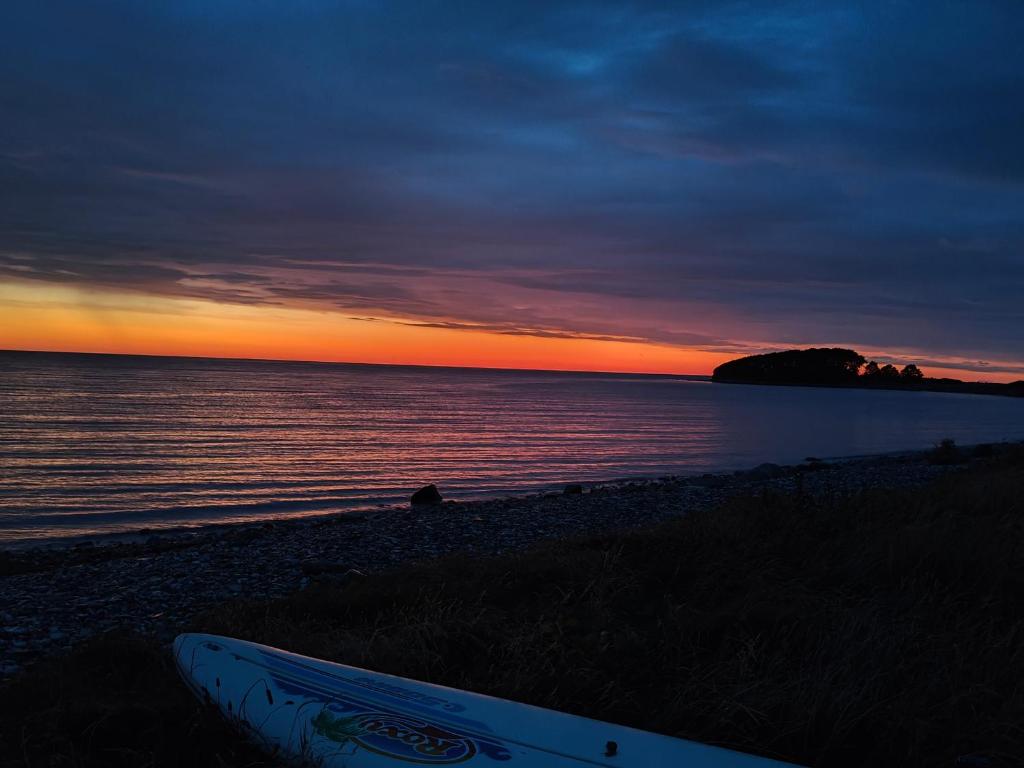 a surfboard sitting on the beach at sunset at Cottage in scenic Langø in Martofte
